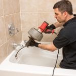 Plumber unclogging a tub drain with an electric auger.