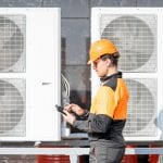 Professional workman in protective clothing adjusting the outdoor unit of the air conditioner or heat pump with digital tablet