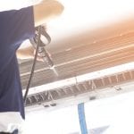 The technicians are cleaning the air conditioner by spraying water. Hand and water spray are cleaning the air conditioner. Focus at air conditioner.