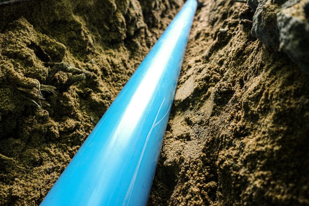 close up on laying PVC water pipe under backfilling sand trench with dark background